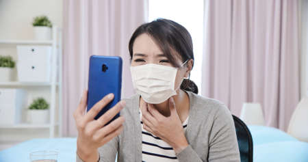 Telemedicine concept-asian female patient consult her health condition to doctor by talking on mobile phone and she has feverの写真素材