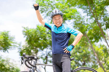 Asian old man wearing helmet and face mask is riding a bicycle in the park-enjoying sport or hobby living healthyの写真素材