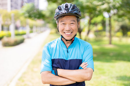 Asian old man wearing helmet and face mask is riding a bicycle in the park-enjoying sport or hobby living healthyの写真素材