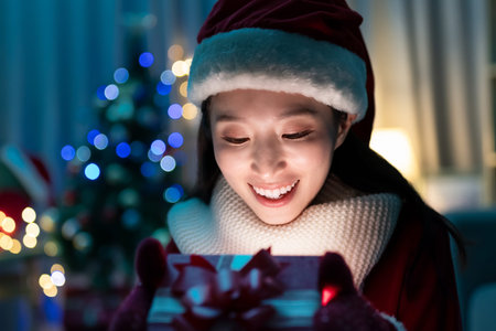 asian young woman wearing christmas clothes has video chat on smart phone and shows present box to...