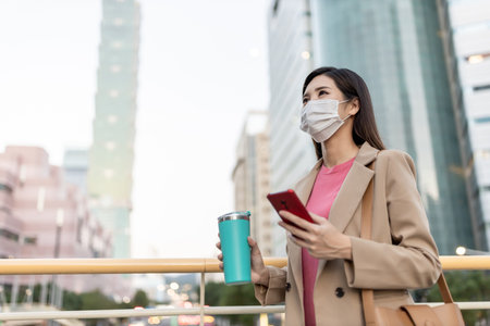 close up of asian woman use smartphone outdoor with face mask while commuting at night