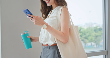 asian young businesswoman use smart phone with reusable eco-friendly ecological cup and bag while commuting in cityの写真素材