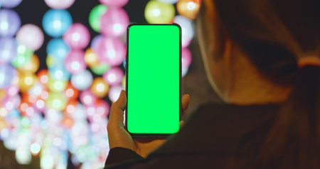 Asian girl see the lanterns and use mobile phone with green screen at night during chinese new yearの写真素材