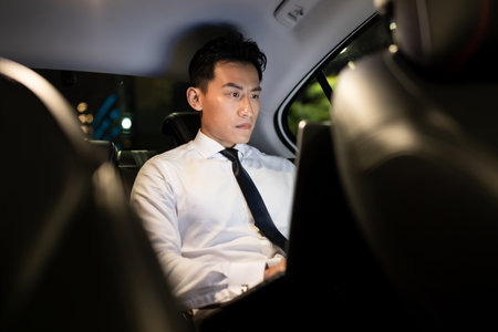 asian successful businessman use smart phone and look out of window in the car at nightの写真素材