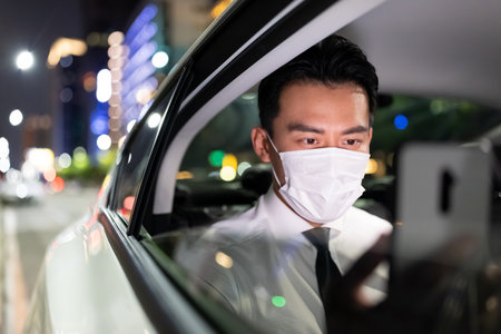 asian businessman wears face mask to avoid infectious diseases coronavirus and uses smart phone while commuting by taxiの写真素材