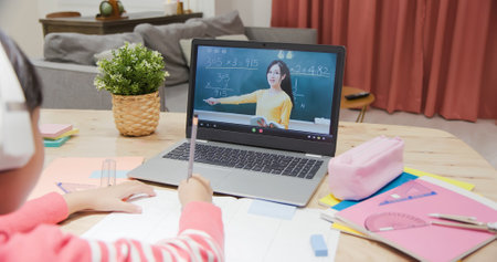 rear view of asian girl is learning math online through listeing to senior male college teacher teaching calculus by laptop at home and write down the noteの写真素材