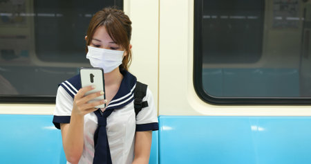 senior high school student girl use mobilephone when commute on mrt and wear face maskの写真素材