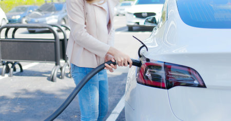 asian woman makes power supply plugged into an electric car being chargedの写真素材
