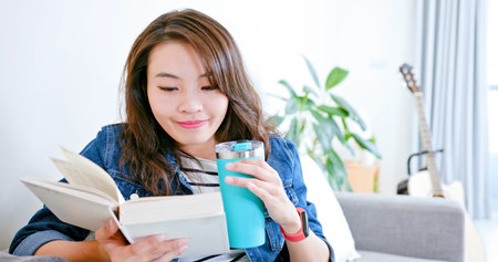 asian woman use reusable eco-friendly ecological bottle to drink while reading books at homeの写真素材