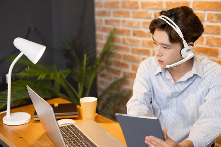 telework concept-Asian businessman wearing headset is joining video meeting by laptop computer and...