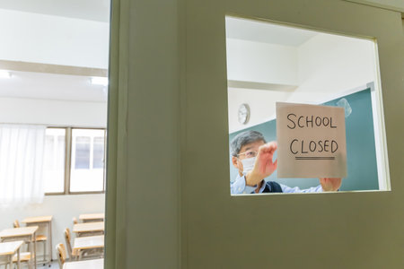asian mature male professor put school closed sign on windows at college classroom to prevent virus spreadingの写真素材