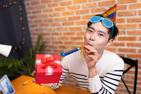 funny asian young man is having video chat online to celebrate birthday and giving present box for his girlfriendの写真素材