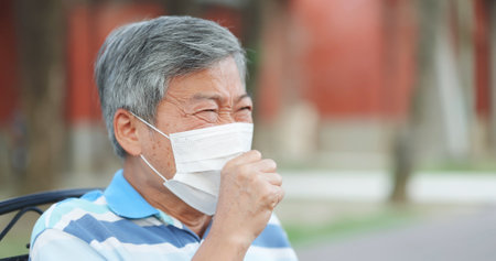 asian elderly man wearing mask get a cold and cough outdoorの写真素材
