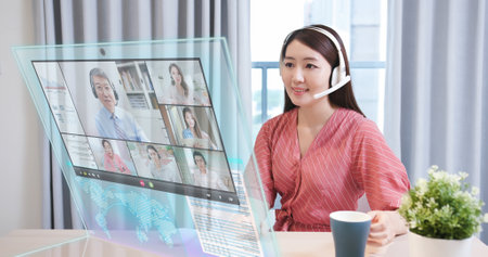 In the near future asian businesswoman join online video meeting while working on transparent display computer at homeの写真素材