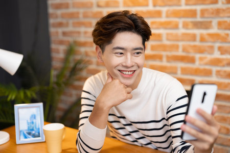 asian young man has video chat by smartphone with friend happily at homeの写真素材