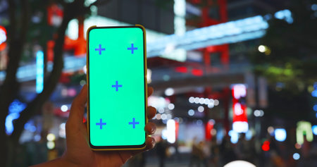 woman holds smartphone with green screen near department store with crowded peopleの写真素材