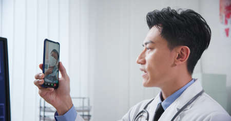 Telemedicine concept-asian young doctor is listening to elder male patient and then talking about his symptom on smart phoneの写真素材