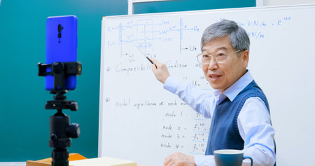 asian mature male professor teach Engineering online through mobile phone in classroom at graduate schoolの写真素材