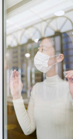 asian young woman wearing face mask stay isolation at home for self quarantine due to epidemic of COVID19-she looks out the windowの写真素材
