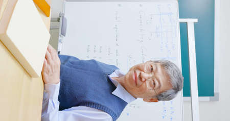 asian mature male professor teach Engineering online through mobile phone in classroom at graduate schoolの写真素材