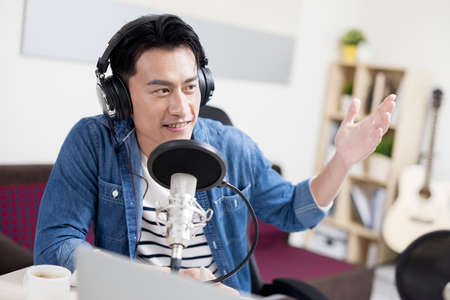 asian man with headphones and microphone recording podcast at studio with laptopの写真素材