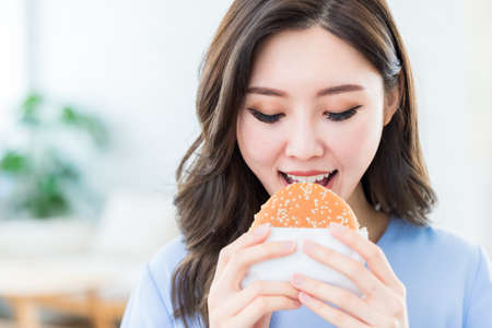 close up of asian woman use hand to grab hamburger and eat fast foodの写真素材