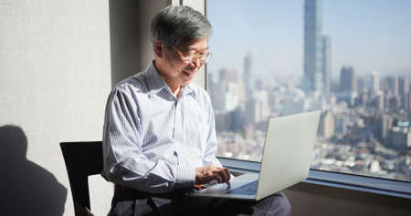 asian senior businessman use laptop to work near window in officeの写真素材