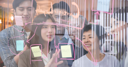 Young businesswoman draws graphs on glass wall with stickers to hold team brainstorming meeting...