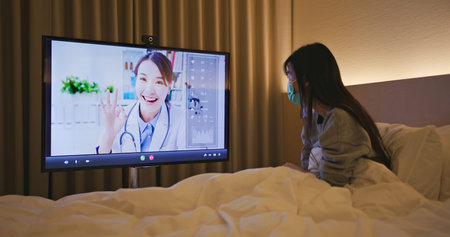 Telemedicine concept-asian woman patient lying on bed has video call with female doctor by big...