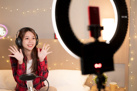 asian girl with microphone has live stream and singing through smartphone in bedroom at homeの写真素材