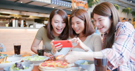 asian young three females friends take the food picture happily in restaurantの写真素材