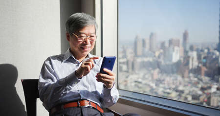 asian senior businessman use smartphone to work near window in officeの写真素材
