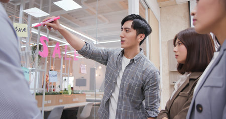 Young businessman writes words on glass wall with stickers to hold team brainstorming meeting about...