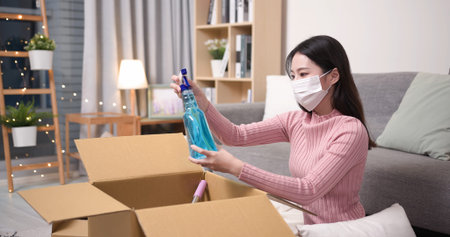 asian young woman wearing surgical face mask is opening online shopping parcel cardboard box with...