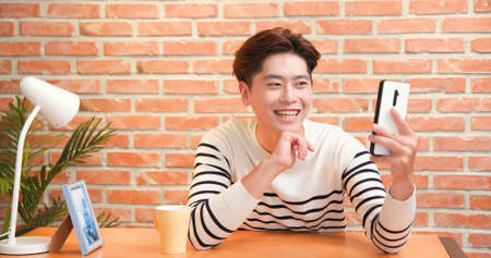 asian young man has video chat by smartphone with friend happily at homeの写真素材