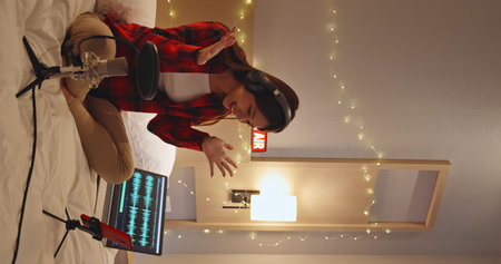 asian woman with microphone has live stream through smartphone in bedroom at home