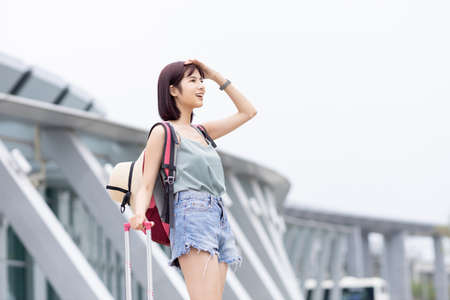 Asian female traveler use smartphone outside the terminal on her summer vacationの写真素材