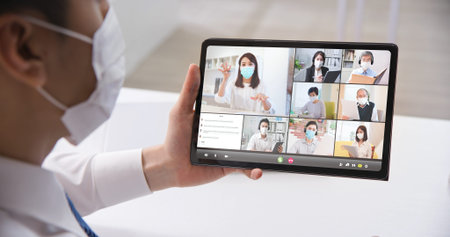 telework concept-rear view of asian businessman wearing face mask is having a group video meeting by...
