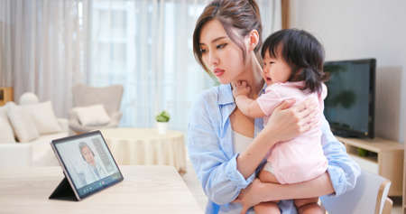 Telemedicine concept-asian young woman has video chat with elder male doctor talking about her daughter sick on digital tabletの写真素材