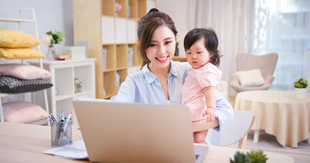 asian business woman works from home with laptop and take care of her daughterの写真素材