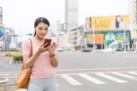 asian woman is standing on the street in city and using smart phone while commutingの写真素材