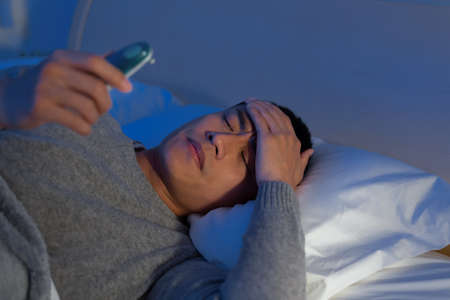 asian man get sick and has a fever while lying at the bed in bedroomの写真素材