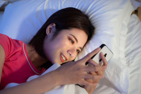 asian woman use smartphone on bed at nightの写真素材