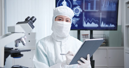 asian biotechnology researcher who is wearing cleanroom clothes has video meeting in the laboratory