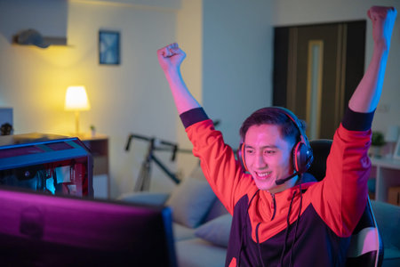 Young Asian Handsome Pro Gamer is Feeling Excited and raising his arms with fist gesture While...