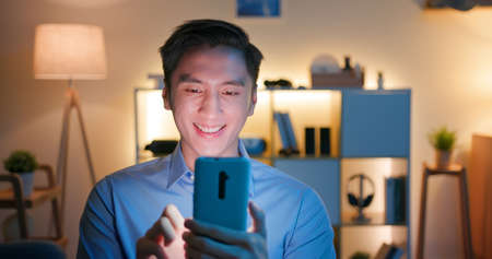 asian man use smart phone and watches something interesting on social media happily at home in the eveningの写真素材