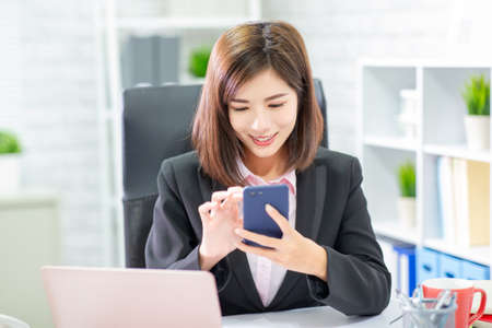 Asian businesswoman use mobile phone happily in the officeの写真素材