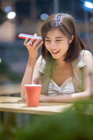Young woman use vocal assistant by phone in coffee shopの写真素材