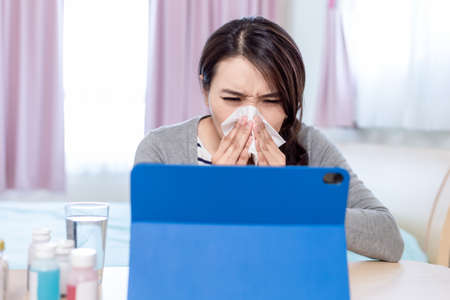 Telemedicine concept-asian female patient consult her health condition to doctor in front of tablet pc and she is sneezingの写真素材