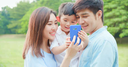 Young asian parent and kid look smartphone happily at parkの写真素材